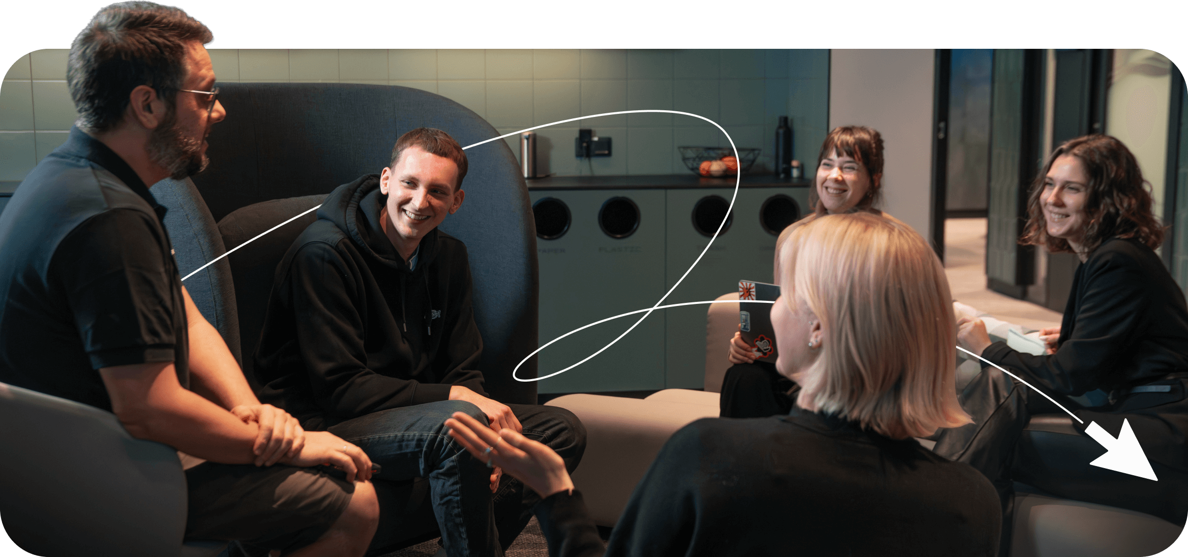 Three women and two men sitting in a circle chatting in a modern office lounge.