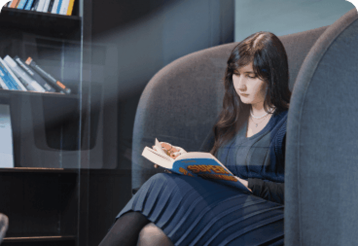A girl on a blue armchair reading a book.