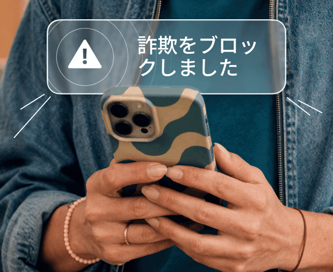 画面に詐欺ブロックの通知アラートが表示されたスマートフォンを持っている人物。