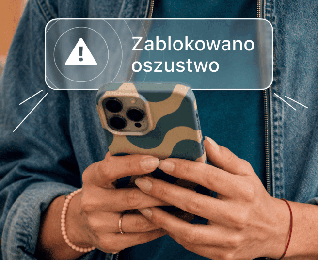 Osoba trzymająca smartfon, na którego ekranie wyświetla się powiadomienie z narzędzia Alert o zablokowaniu oszustwa.