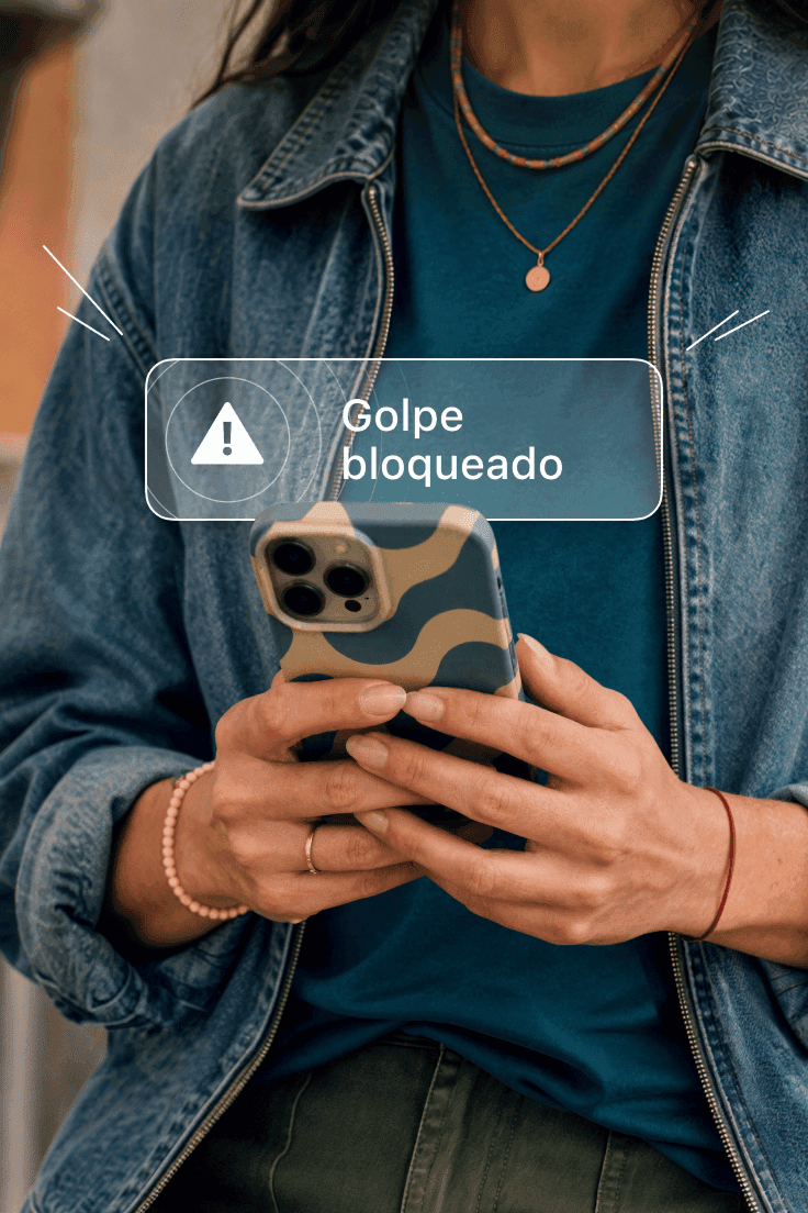 Pessoa segurando um smartphone mostrando um alerta de "Golpe bloqueado" na tela.
