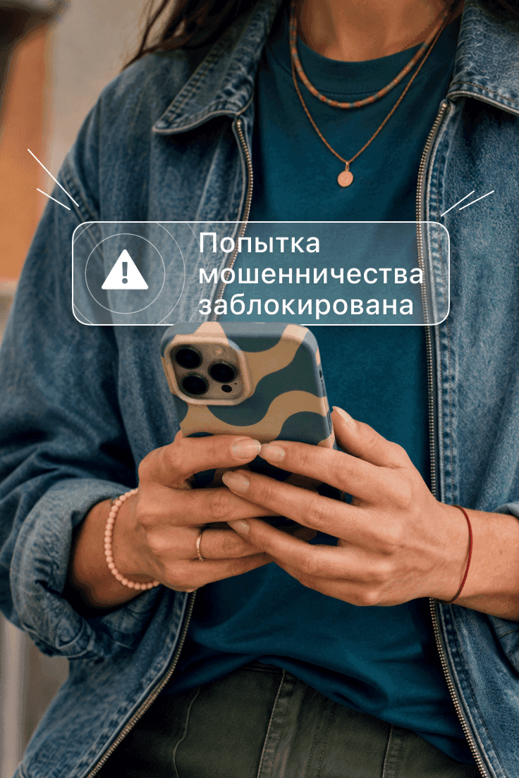 Человек держит смартфон, на экране которого отображается оповещение «Мошенничество заблокировано».