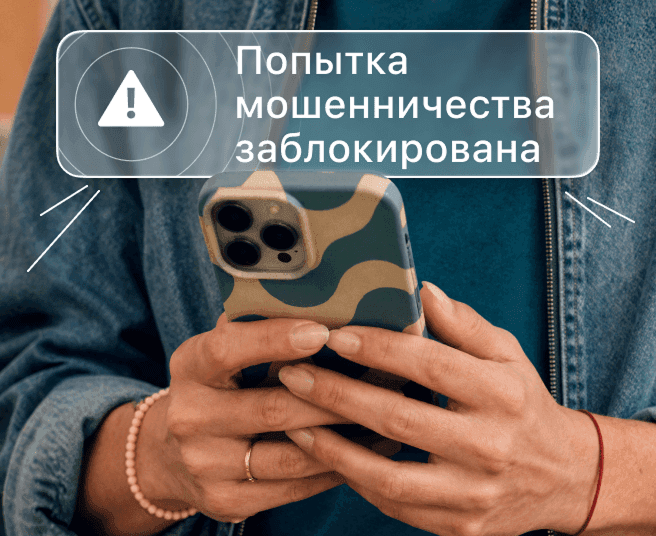 Человек держит смартфон, на экране которого отображается оповещение «Мошенничество заблокировано».