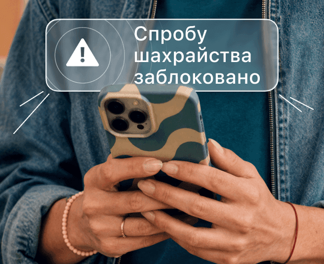 Людина тримає смартфон зі сповіщенням про блокування шахрайства на екрані.