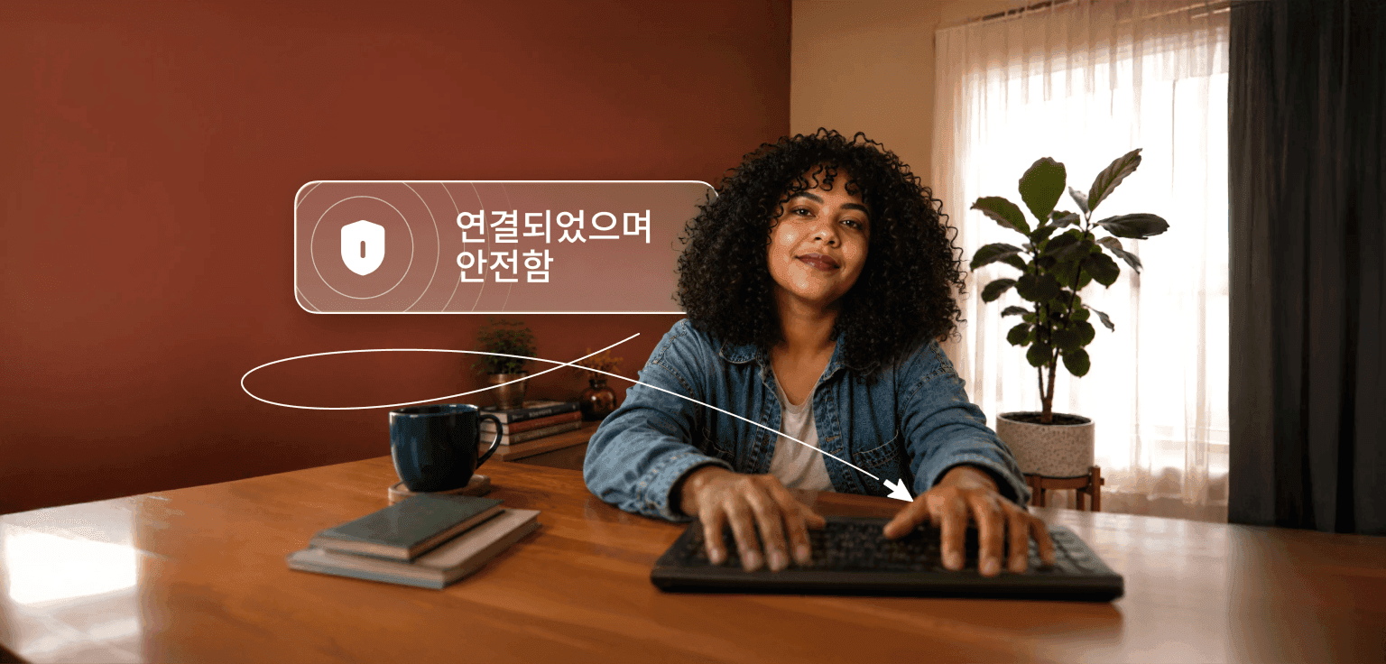 곱슬머리의 한 사람이 책상에서 노트북에 타이핑하고 있으며 그 위에는 '연결되었으며 안전합니다'라는 말풍선이 있는 모습.