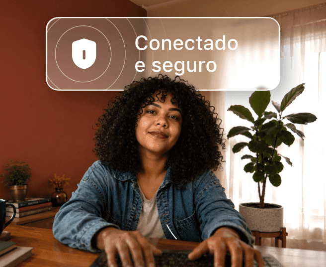 Pessoa com cabelo cacheado digita em um notebook em uma mesa com um balão de fala acima dela com o texto "Conectado e seguro".