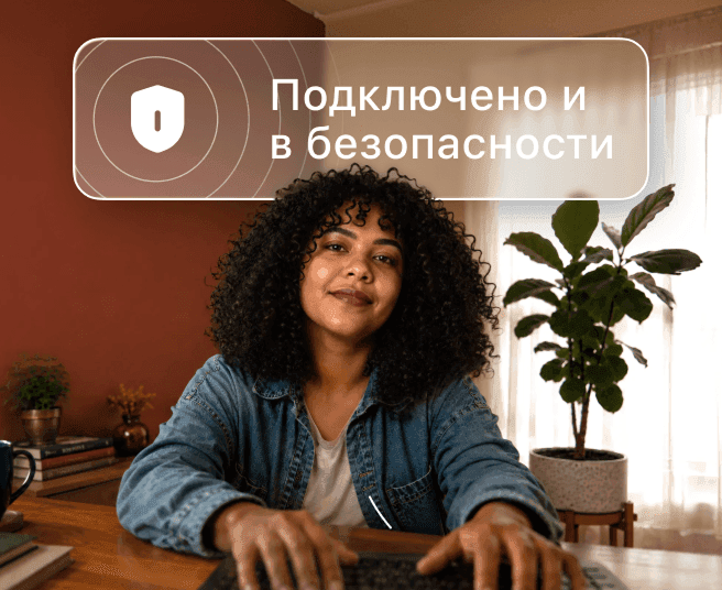 Человек с кудрявыми волосами печатает на ноутбуке за столом; над ним облачко с текстом «Подключено и безопасно».