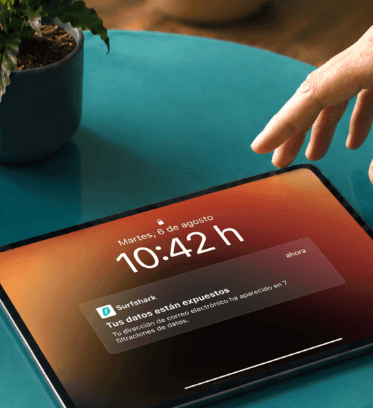 Una mano se acerca a una tableta que muestra una notificación con el texto: «Tus datos están expuestos».