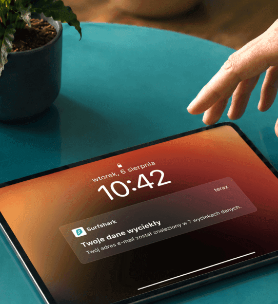 Dłoń sięgająca po tablet wyświetlający powiadomienie o treści „Twoje dane zostały ujawnione”.