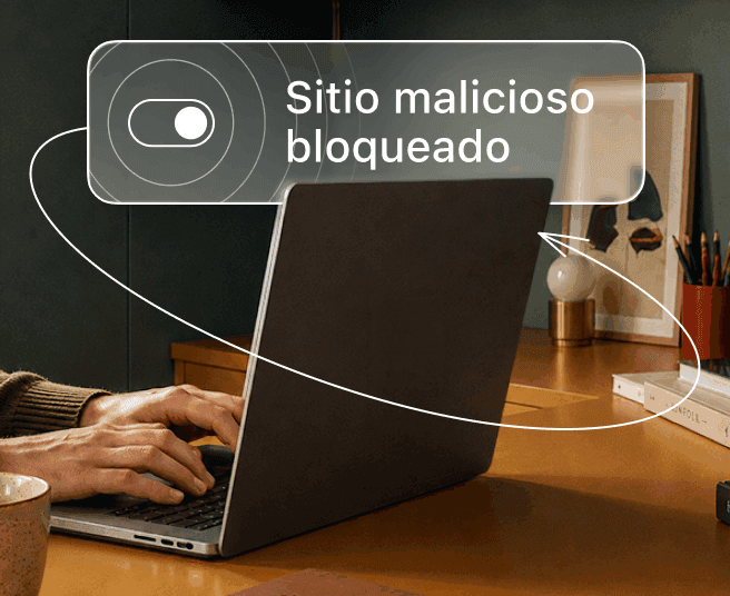 Una persona escribe en un portátil mientras una superposición digital muestra un interruptor y el texto «Sitio malicioso bloqueado».