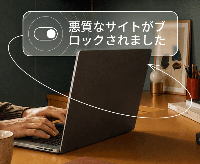 デジタルオーバーレイにトグルスイッチと「悪意のあるサイトがブロックされました」というテキストが表示されている中で、ノートパソコンでタイピングしている人物。