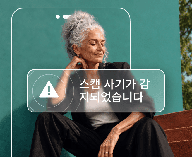 청록색 벽을 배경으로 앉아 있는 회색 머리의 여성이 '스캠 사기 감지됨' 경고 알림이 표시된 휴대폰 윤곽선으로 일부 가려져 있는 모습.