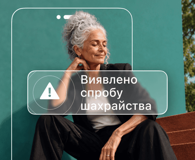 Жінка із сивим волоссям сидить на тлі бірюзової стіни, частково закрита контуром телефону зі сповіщенням про виявлення шахрайства.