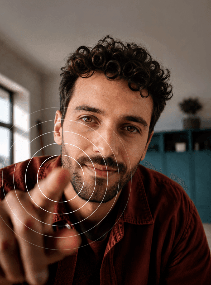 Un homme aux cheveux bouclés et barbu, tendant la main vers la caméra, avec des cercles blancs concentriques centrés sur son doigt.