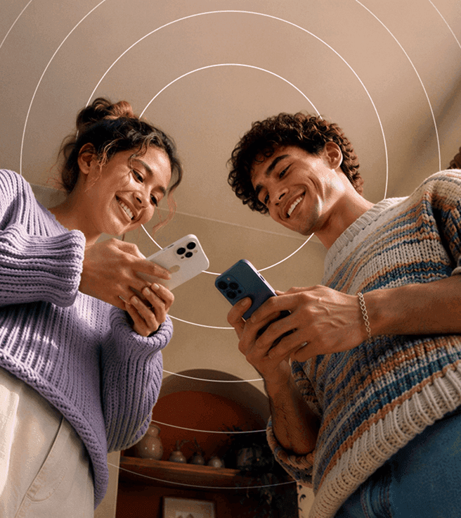 Un homme et une femme souriants, portant des pulls, se tiennent côte à côte, chacun tenant un téléphone sous une illustration représentant des cercles concentriques.