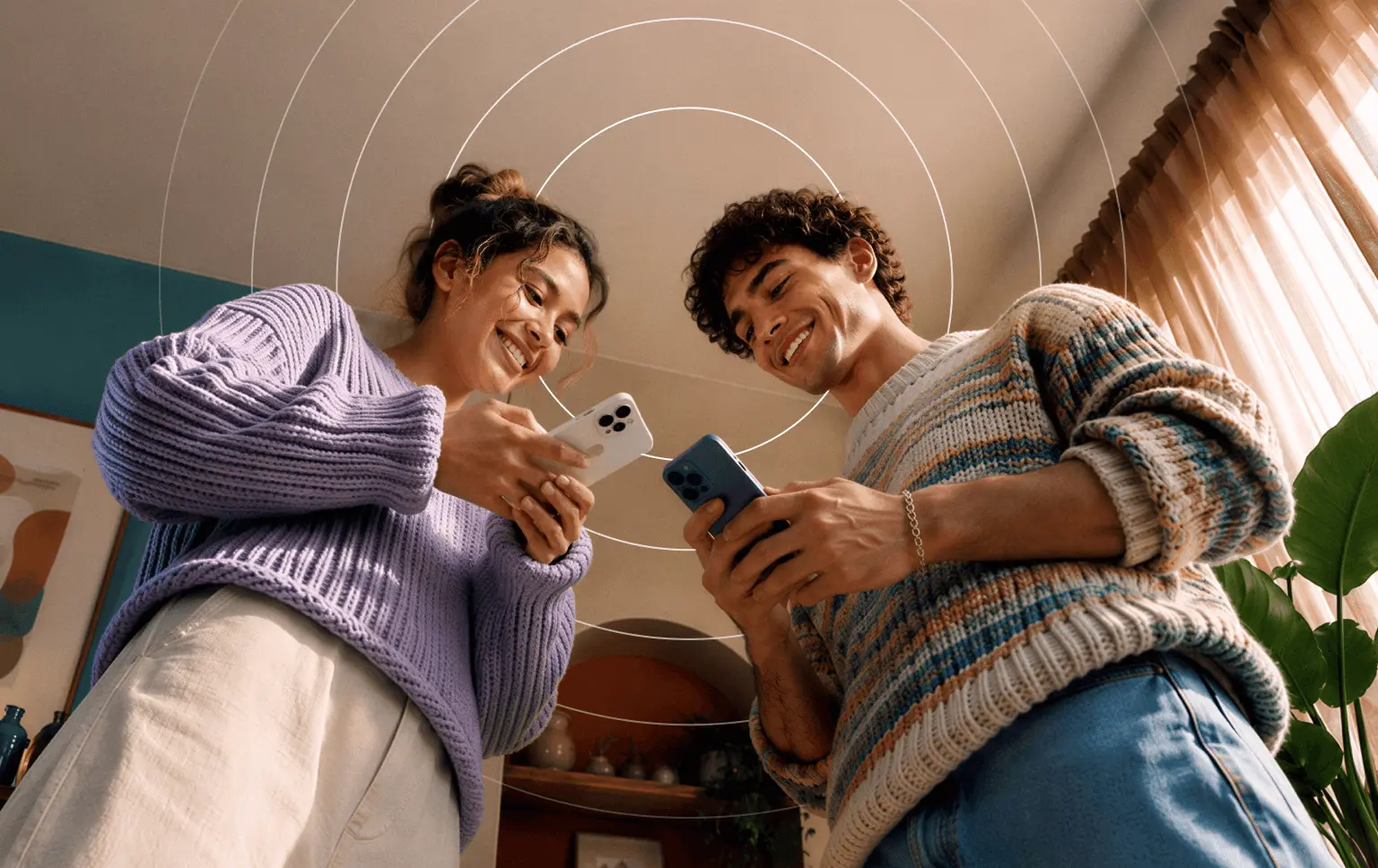 Un homme et une femme souriants, portant des pulls, se tiennent côte à côte, chacun tenant un téléphone sous une illustration représentant des cercles concentriques.