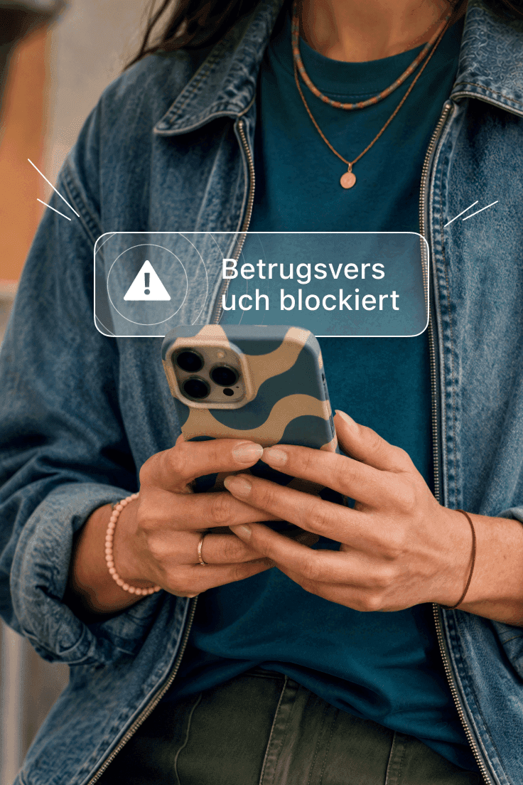 Person hält ein Smartphone mit einem Benachrichtigungs-Alert „Betrug blockiert“ auf dem Bildschirm.
