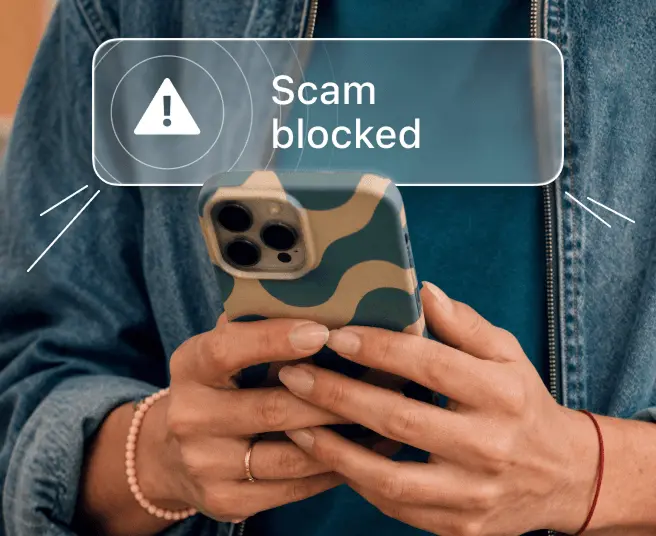 Person holding a smartphone with a Scam blocked notification alert on the screen.