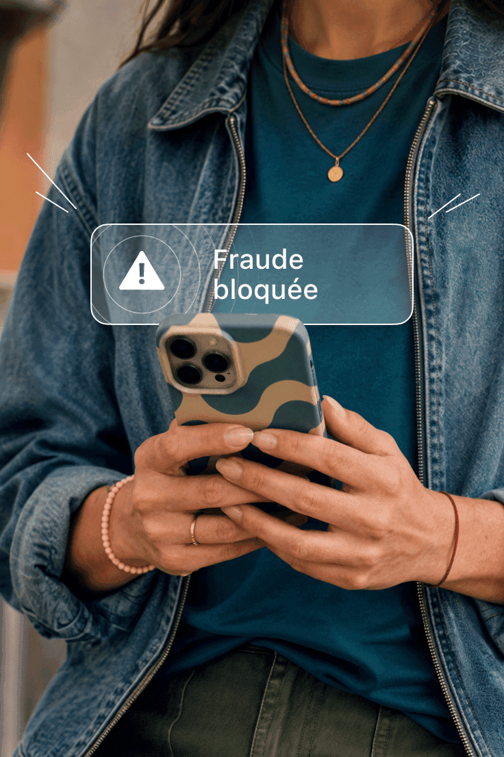 Une personne tenant un téléphone affichant une notification indiquant qu’une tentative de fraude a été bloquée.
