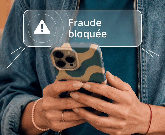 Une personne tenant un téléphone affichant une notification indiquant qu’une tentative de fraude a été bloquée.