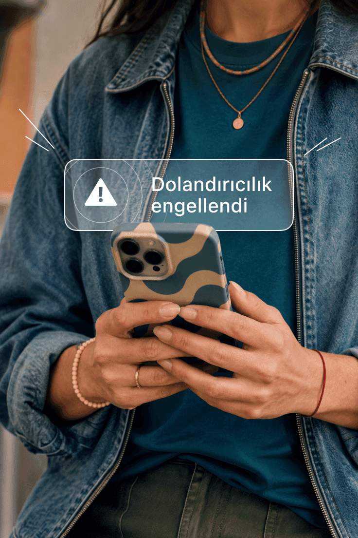 Ekranında 'Dolandırıcılık engellendi' bildirim uyarısı bulunan bir akıllı telefonu tutan kişi.