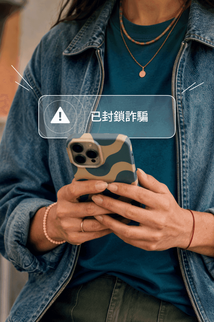 人物手持智能手機,螢幕顯示「詐騙已攔截」通知提示。
