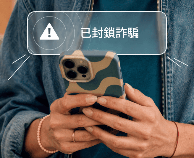人物手持智能手機,螢幕顯示「詐騙已攔截」通知提示。