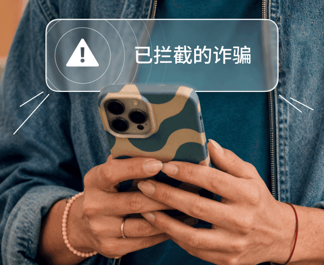 一个人拿着智能手机,屏幕显示“诈骗已拦截”通知警示。