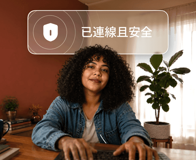 一位捲髮人士正坐在書桌前用筆記型電腦打字,上方有一個寫著「已連線並安全」的對話氣泡。