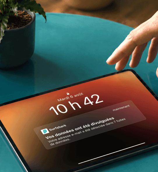 Une main se tendant vers une tablette affichant une notification indiquant « Vos données sont exposées ».