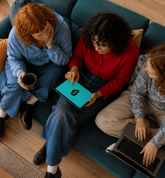 Trois personnes assises sur un canapé regardent l’écran d’une tablette sur lequel est affiché le logo de Surfshark.