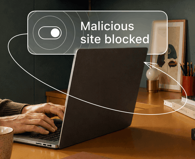 A person types on a laptop while a digital overlay displays a toggle switch and the text Malicious site blocked.