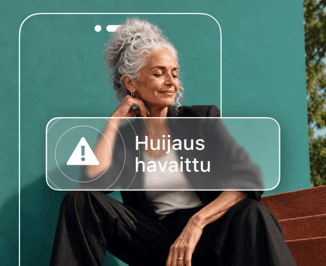 Harmaahiuksinen nainen istuu sinivihreää seinää vasten osittain puhelimen ääriviivojen peittämänä, ja puhelimen ilmoituksessa lukee ”Huijaus havaittu”.