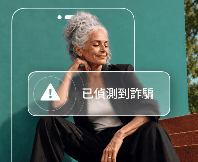 一名灰髮女士倚著深青色牆壁而坐,身體部分被手機輪廓遮擋,畫面顯示「偵測到詐騙」提示。
