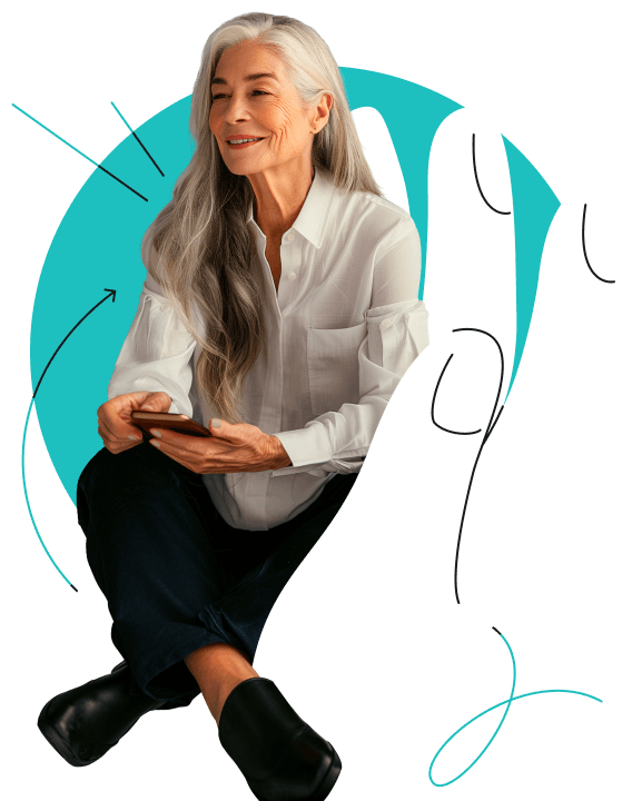 A smiling woman with long gray hair, wearing a white shirt and dark pants, sitting on a large white hand and holding a phone.