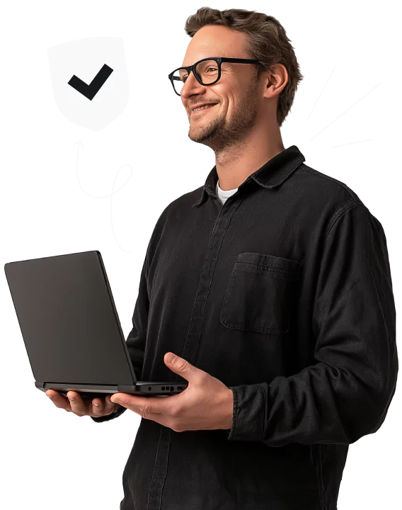 A smiling man with glasses and a black shirt holding a laptop, looking to the side, and standing by a checkmarked shield.
