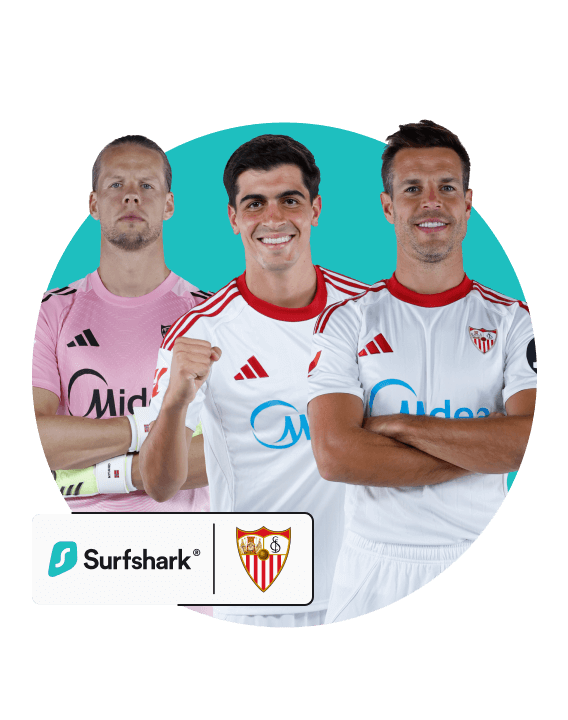 Three Sevilla FC soccer players, two in a white kit and one in a pink goalie jersey, by the club crest and Surfshark logo.
