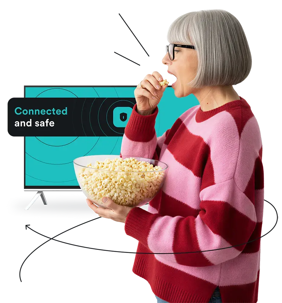 A woman in a pink and red sweater eating popcorn in front of a TV, with a message Connected and safe on screen.