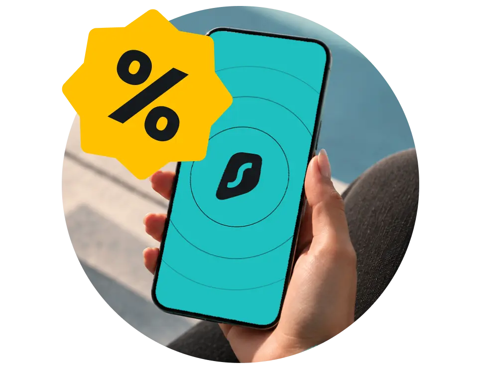 Hand holding a smartphone displaying a teal background and black Surfshark logo, overlaid by a yellow percent sign badge at the top left.